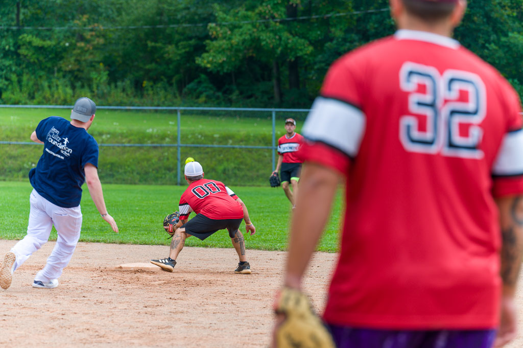 Runner sliding into second base as a player waits to make a catch from the outfield.