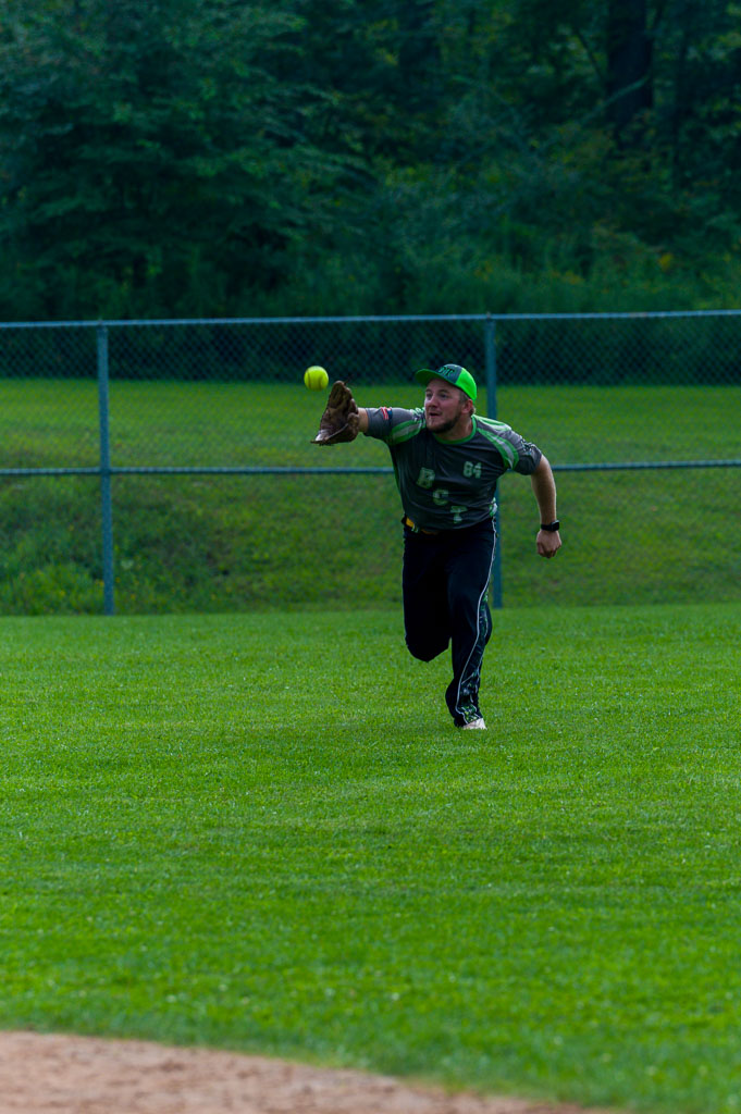 Outfielder stretches forward to catch fly ball.