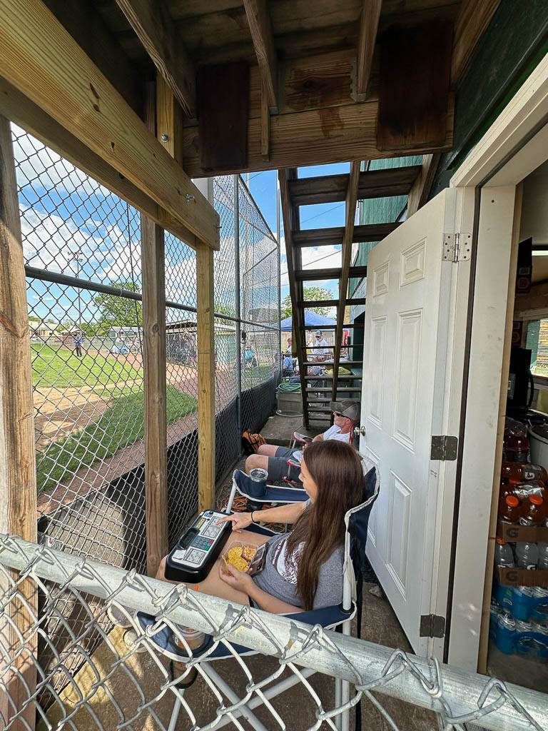 Scoreboard operator watches game from behind the fence.